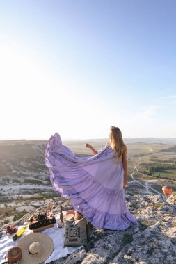 Havalı balonlarla vadi manzaralı piknik yapan zarif elbiseli güzel bir kadının açık hava fotoğrafı.