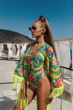 Plaj kulübünde yüzme havuzu ve deniz manzaralı pozlar veren siyah saçlı güzel seksi bir bayram fotoğrafı.