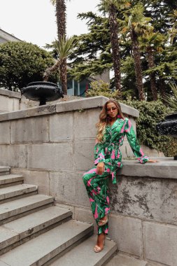 Sarışın, zarif elbiseli, antika tarihsel bir yerde poz veren güzel bir kadının açık hava fotoğrafı.