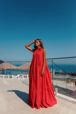 Sahil kulübünde deniz manzaralı şık bir şekilde poz veren güzel, sarışın ve seksi bir kadının açık hava fotoğrafı.