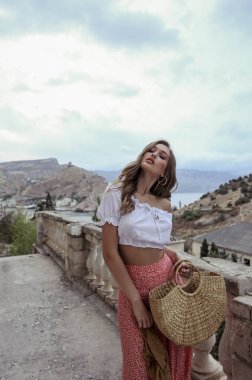 Güzel doğa arka planında, zarif elbiseli ve aksesuarlı, sarışın güzel bir kadının moda fotoğrafı.