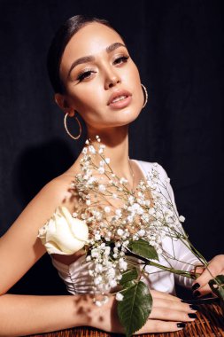 Moda stüdyosunda güzel bir kadın resmi. Koyu renk saçlı, zarif elbiseli, çiçeklerle poz veren.