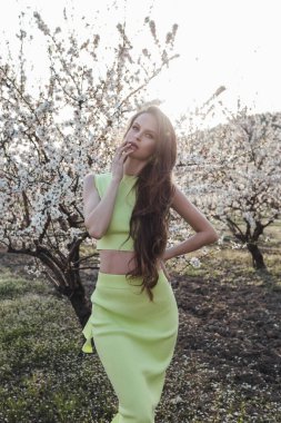 Güzel, siyah saçlı, zarif elbiseli, baharda çiçek açan bahçede poz veren güzel bir kadının moda fotoğrafı.