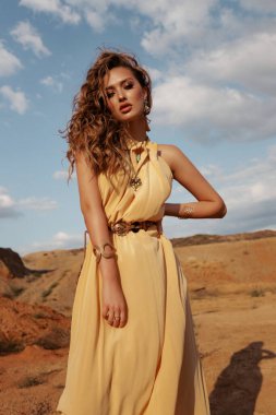 Çölde poz veren güzel, sarı saçlı, şık elbiseli bir kadının moda fotoğrafı. 