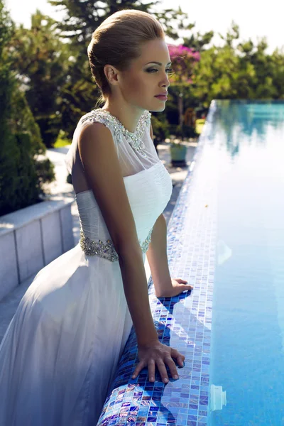 Beautiful bride in wedding dress posing beside a swimming pool — Stock Photo, Image