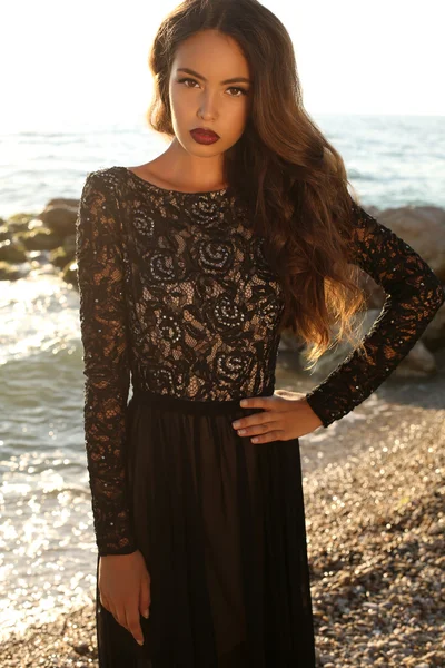 Hermosa morena en negro vestido de encaje posando en la playa — Foto de Stock