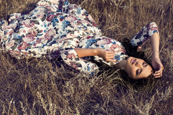 Hermosa mujer con pelo negro en vestido colorido acostado en el campo —  Fotos de Stock