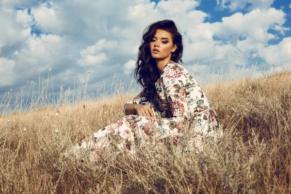 Vacker kvinna med mörkt hår i färgglada klänning poserar i fältet — Stockfoto