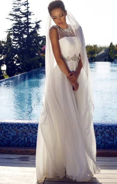 Beautiful bride in elegant dress posing beside s swimming pool — Stock Photo, Image