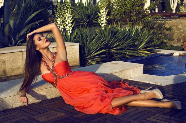 Красива брюнетка в розкішній червоній сукні позує в парку — стокове фото