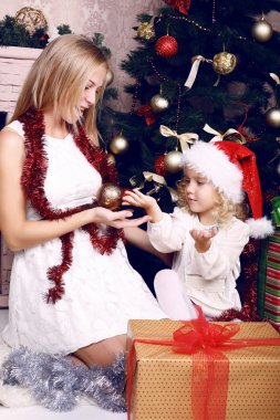 Noel Baba'nın şapkalı bir Noel ağacı yanında annesiyle oynayan sevimli küçük kız