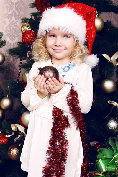 Мила маленька дівчинка в капелюсі Санти прикрашає ялинку — стокове фото