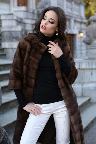 Bela mulher com cabelo escuro no luxuoso casaco de pele posando nas escadas — Fotografia de Stock