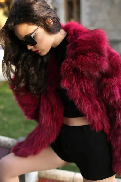 Sexy girl with dark hair in fashion red fur coat and sunglasses — Stock Photo, Image