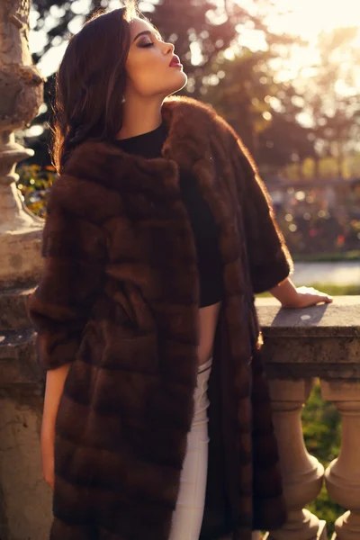 Beautiful brunette woman in luxurious fur coat posing in autumn park — Stock Photo, Image