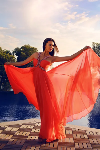 Bela mulher em vestido vermelho luxuoso posando ao lado de uma piscina — Fotografia de Stock