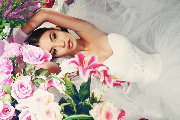 Mooie bruid in elegante jurk poseren onder bloemen — Stockfoto