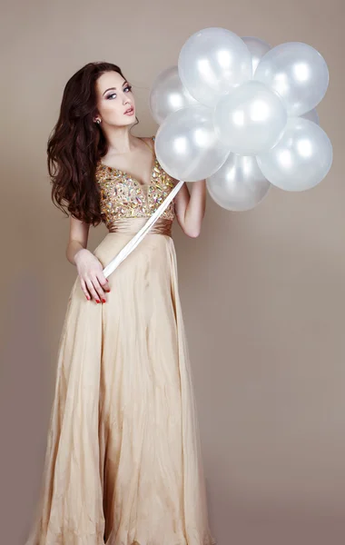 Fille aux cheveux foncés portant une robe de luxe, tenant des ballons blancs — Photo