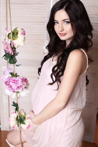 Mulher grávida com cabelo escuro longo posando no interior acolhedor — Fotografia de Stock