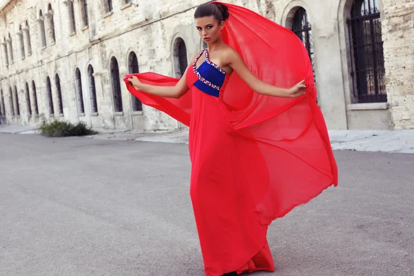 Beautiful woman with dark hair in luxurious red dress posing in old castle — Stock Photo, Image