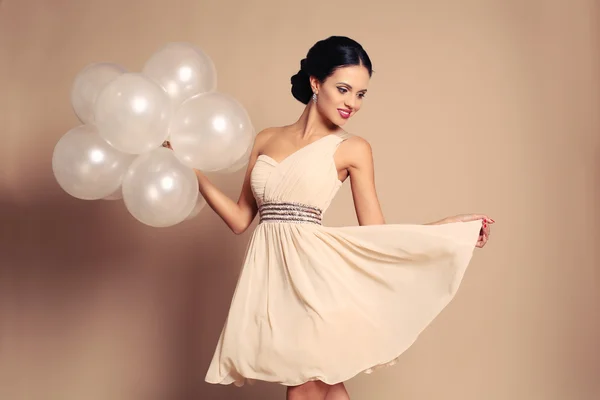 Menina sensual com cabelo escuro em vestido bege elegante segurando balões brancos — Fotografia de Stock