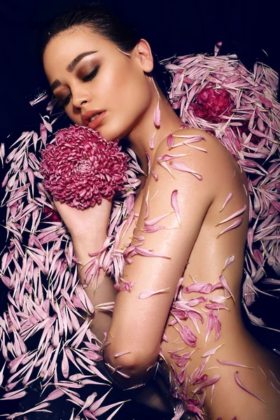 Woman with dark hair lying naked in petals of chrysanthemum in bathtub — Stock Photo, Image