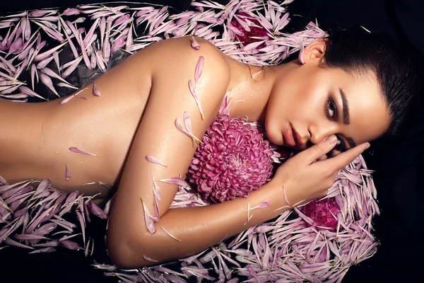 Beautiful woman with dark hair lying in petals of chrysanthemum in bathtube — Stock Photo, Image