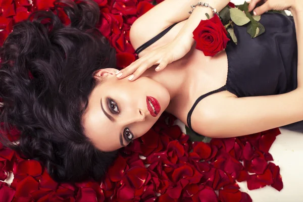 Schöne junge Frau mit dunklen Haaren auf Rosenblättern liegend — Stockfoto