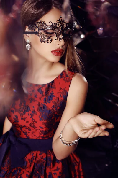 Prachtige vrouw met donker haar in elegante jurk en masker — Stockfoto