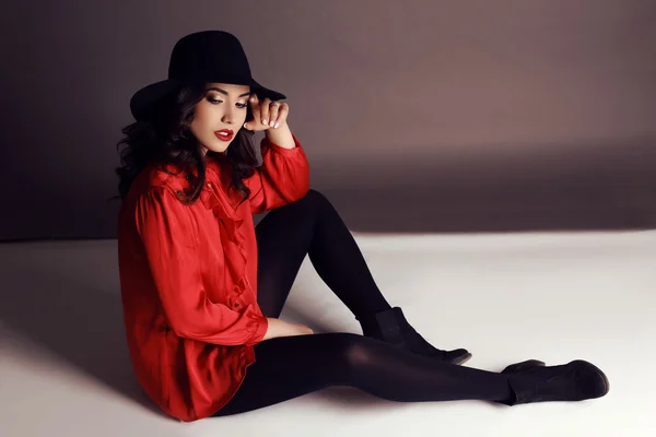Belle fille aux cheveux foncés en chemisier rouge élégant et chapeau noir — Photo