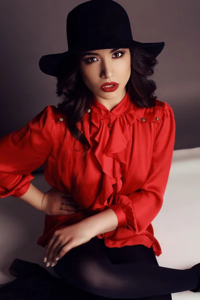 Όμορφη κοπέλα με σκούρα μαλλιά σε κομψό κόκκινη μπλούζα και μαύρο καπέλο — Φωτογραφία Αρχείου