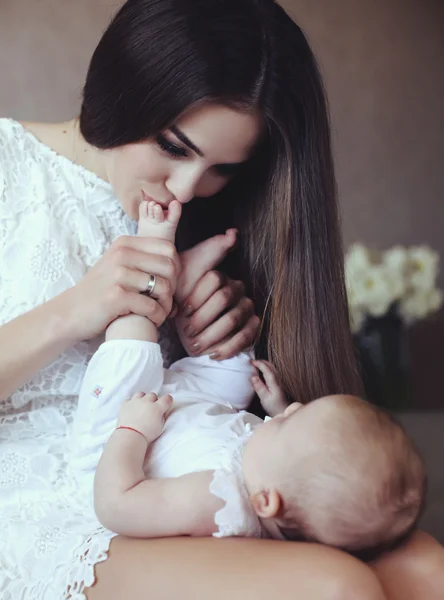 Schöne junge Mutter mit langen dunklen Haaren posiert mit ihrem kleinen entzückenden Baby — Stockfoto