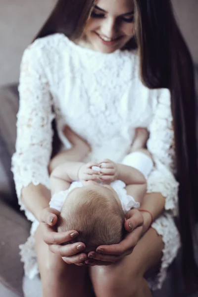 Όμορφη νεαρή μητέρα με μακριά σκούρα μαλλιά που θέτει με την μικρή αξιολάτρευτο μωρό — Φωτογραφία Αρχείου