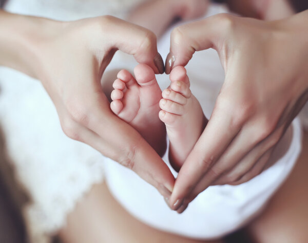  baby feets in mom hands holding them in heart shape  