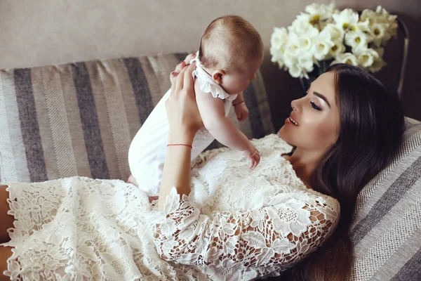 Bela jovem mãe com longos cabelos escuros posando com seu pequeno bebê adorável — Fotografia de Stock