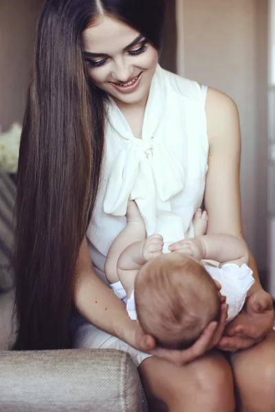 Bela jovem mãe com longos cabelos escuros posando com seu pequeno bebê adorável — Fotografia de Stock