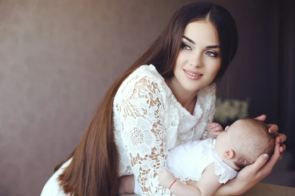 Bela jovem mãe com longos cabelos escuros posando com seu pequeno bebê adorável — Fotografia de Stock