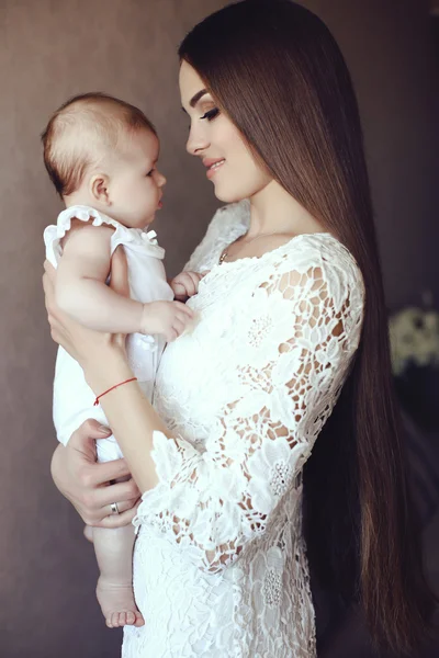 Hermosa joven madre con el pelo largo y oscuro posando con su pequeño bebé adorable — Foto de Stock