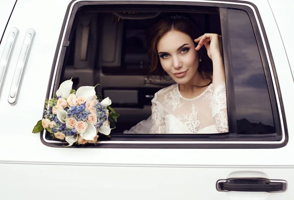 Sensual bride with dark hair in luxurious wedding dress posing in car — Stock Photo, Image