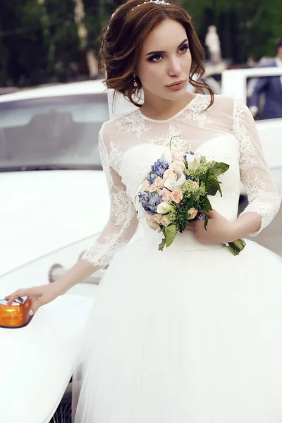 Sensual bride with dark hair in luxurious wedding dress posing beside car — Stock Photo, Image