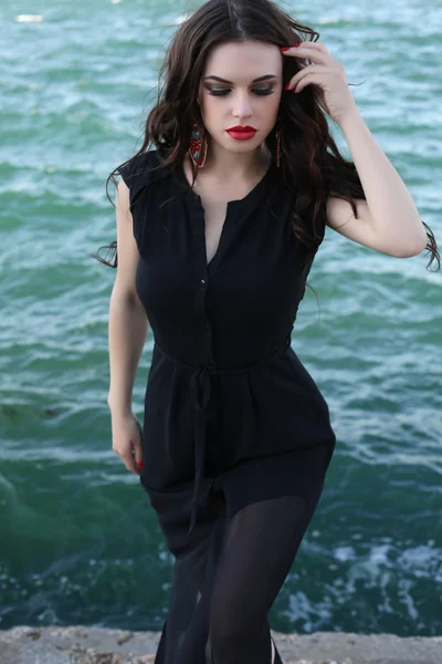 Sensual woman in elegant black dress posing beside sea — Stock Photo, Image