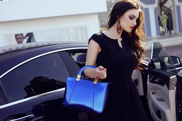 Frau in elegantem Kleid mit Tasche posiert neben einem luxuriösen Auto — Stockfoto