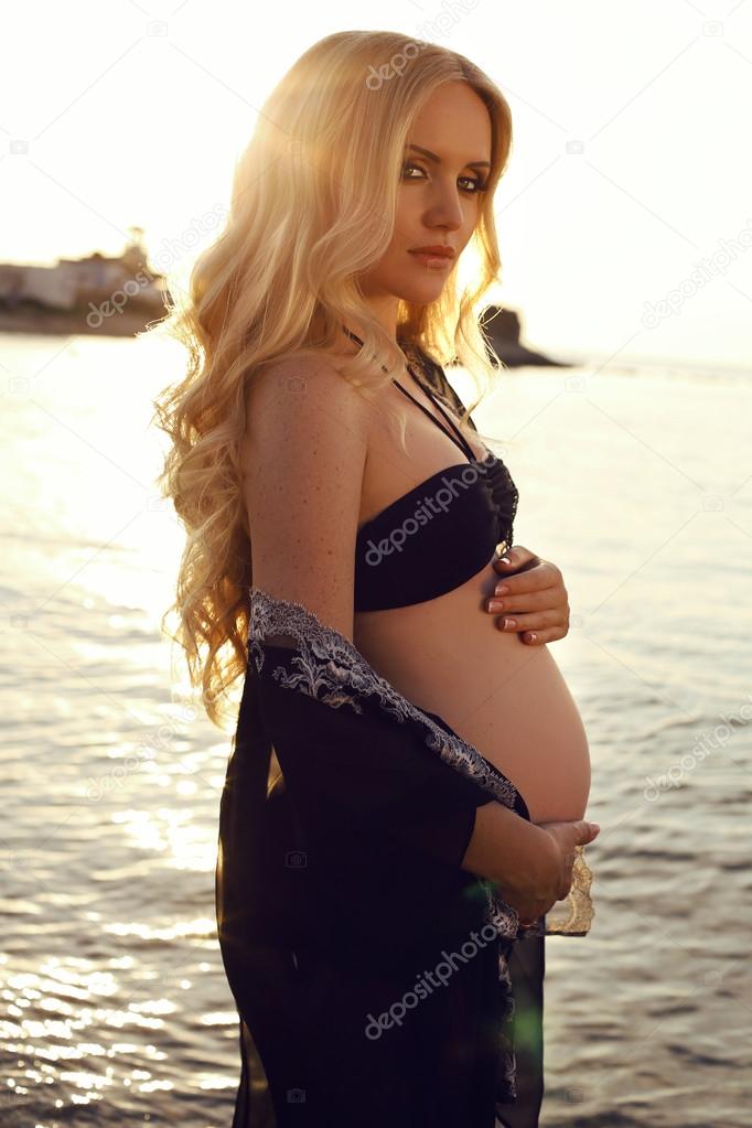 beautiful pregnant woman with long blond hair posing on sunset beach  