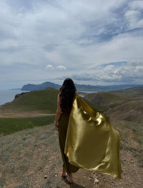 Güzel, siyah saçlı, lüks elbiseli, arka planda dağlarla tepede poz veren güzel bir kadının moda fotoğrafı.