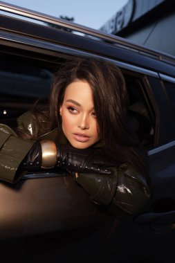 Güzel, şehvetli, siyah saçlı, zarif deri ceketli ve sokakta poz veren aksesuarlı bir kadının moda fotoğrafı.