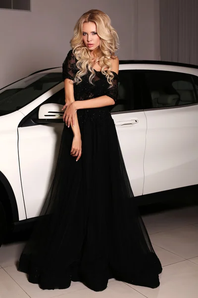 Mujer con el pelo largo y rubio lleva vestido de lujo, posando al lado del coche blanco — Foto de Stock