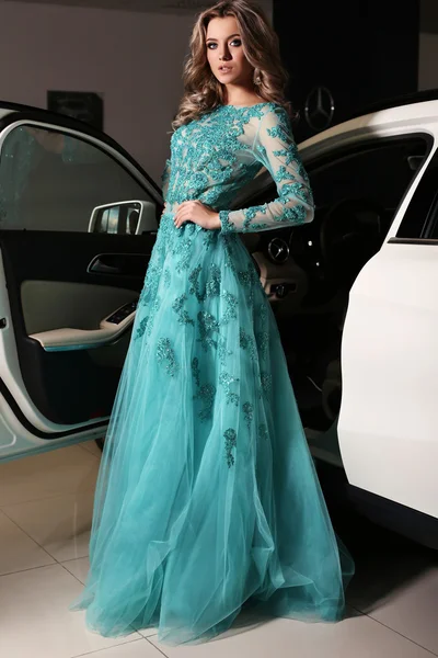Woman with long blond hair wears luxurious dress,posing beside white car — Stockfoto