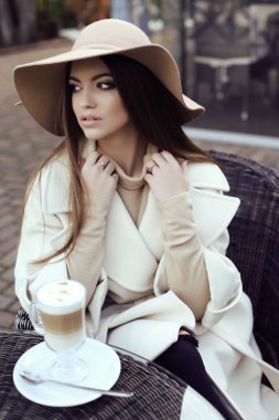 karanlık düz saçlı Glamour kızı şık şapka ile lüks bej bir palto giyiyor 