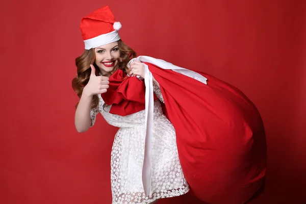 Chica joven con sonrisa encantadora, en Santa sombrero, con bolsa grande con regalos —  Fotos de Stock