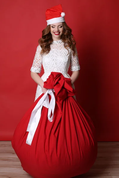 Chica joven con sonrisa encantadora, en Santa sombrero, con bolsa grande con regalos —  Fotos de Stock